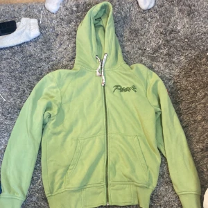 Ljusgrön hoodie Peak Performance S - Ljusgrön hoodie från Peak Performance med broderad logga på bröstet och coolt märke på ärmen. Tröjan har dragkedja, huva med snörning och ribbade muddar. 