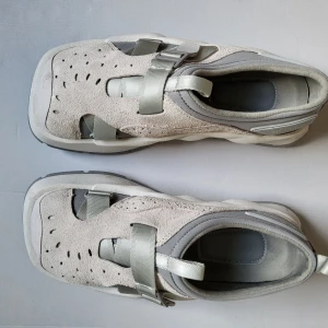 Grå sandaler från Eytys i mocka / Eytys Oasis Suede - Chunky sandaler från Eytys i ljusgrå mocka med breda band och coola utskärningar. Snygg perforerad ovandel, robust sula och detaljer i syntet. Perfekta för dig som gillar streetstyle och vill ha något unikt på fötterna.