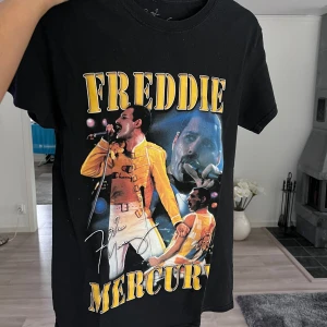 Freddie Mercury-t-shirt - Svart t-shirt med stort tryck av Freddie Mercury. Officiell merch, klassisk rund hals och korta ärmar. Tillverkad i 100% bomull, perfekt för dig som älskar Queen ❤️👑 Önskar du veta exakta mått? Tveka inte att höra av dig!