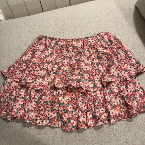 Blommig volangkjol - Charmig kortkjol med blommigt mönster i rosa, rött och grönt. Kjolen har volanger som ger en lekfull look. Perfekt för sommarens äventyr! Pris kan diskuteras och jag är villig till att sänka priset!!!