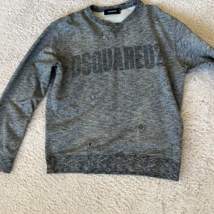 Grå tröja från Dsquared2 - Säljer en grå tröja från Dsquared2 med tryck på framsidan. Tröjan har långa ärmar och en avslappnad stil. Perfekt för en casual look.