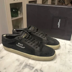 Saint Laurent skor - Snygga svarta sneakers från Saint Laurent med vit logga på sidan strl 43. Skorna har en klassisk design med snörning och en bekväm sula. Perfekta för en stilren look. Skick 4 eller 5/10. finns slitage men syns nästan inte när dom är på. Skriv för mer info mvh! 