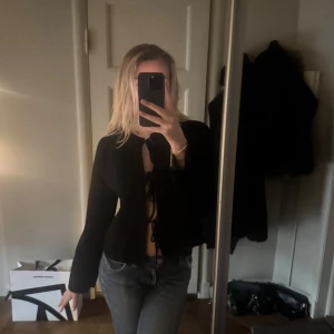Svart  tröja med knyt - Säljer en stilren svart tröja med knyt framtill. Tröjan har långa ärmar och en enkel design som passar perfekt till jeans eller kjol. Perfekt för en kväll ute eller en avslappnad dag.