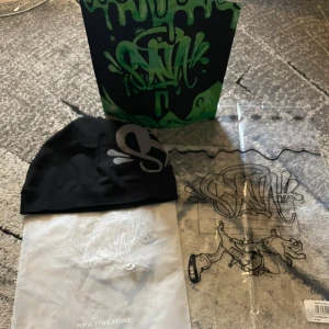 Syna world mössa - Snygg svart mössa från SYNA med ett stort grått tryck framtill. Perfekt för att hålla stilen när det är kallt ute. Kommer i en cool förpackning med matchande design.