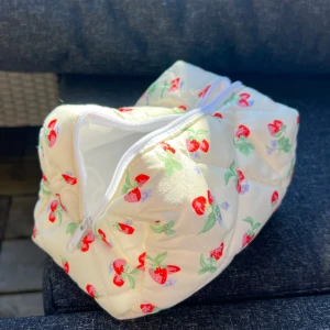 Vit quiltad necessär med jordgubbsmönster - Charmig vit necessär med quiltad design och ett sött jordgubbsmönster. Perfekt för att förvara smink eller andra småsaker. Den har en praktisk dragkedja för enkel öppning och stängning. Så himla fin. 