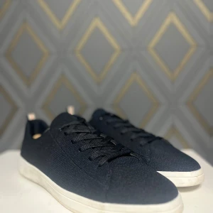 Marinblåa sneakers med vit sula - Snygga marinblåa sneakers från primark med vit sula och diskret snörning. De har en stilren design med en röd och vit randdetalj på hälen. Perfekta för en avslappnad stil.
