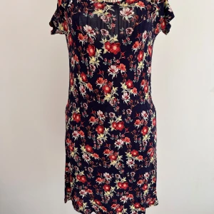 Blommig klänning från Divided - Säljer en söt blommig klänning från Divided, Stl 36. Den har en mörkblå bas med röda och vita blommor. Klänningen har tunna axelband och små ärmar som sitter på sidan av axlarna. Klänningen är mjuk och väldigt skön. Perfekt för en somrig look! 🌸