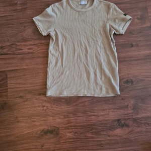 Beige ribbad t-shirt - Säljer en beige ribbad t-shirt från Bershka. Den har en klassisk rund hals och korta ärmar. En liten etikett på ena ärmen. Storlek xs