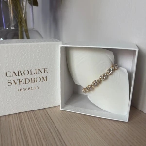 Guldarmband från Caroline Svedbom - Elegant guldarmband från Caroline Svedbom med gnistrande stenar och pärlor. Perfekt för att ge en lyxig touch till din outfit. Kommer i originalförpackning.