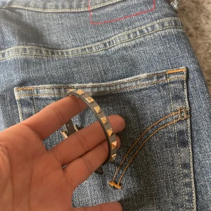 Valentino armband  - Snyggt grått armband med guldnitar och ett fyrkantigt guldfärgat spänne. Perfekt för att ge en edgy touch till din outfit. 