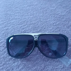 Svarta solglasögon - Snygga svarta solglasögon med guldiga detaljer på bågarna. De har en klassisk rektangulär form och mörka linser. Perfekta för en stilren look.