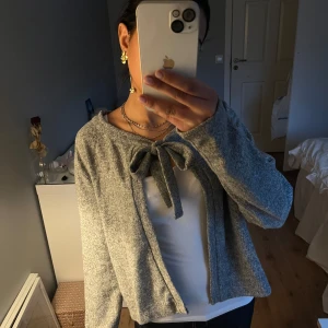 Grå kofta med knytband - Säljer en stilren grå kofta med knytband framtill. Perfekt för lager-på-lager och ger en mysig känsla. Passar bra till både vardag och mer uppklädda tillfällen. Mycket bra skick!