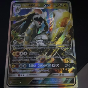 Kommo-o GX Pokémonkort - Säljer ett Kommo-o GX Pokémonkort med 240 HP. Kortet har attacker som Adamantine Press och Ultra Uppercut GX. Perfekt för samlare eller spelare som vill förstärka sin kortlek. Kortet har en glänsande yta och är i standard Pokémonkort-storlek.