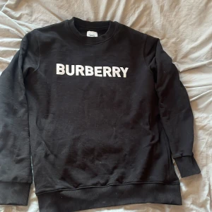 Svart sweatshirt från Burberry - Säljer en svart sweatshirt från Burberry med deras ikoniska logga i vitt på bröstet. Kan absolut diskutera pris, kom bara med förslag 