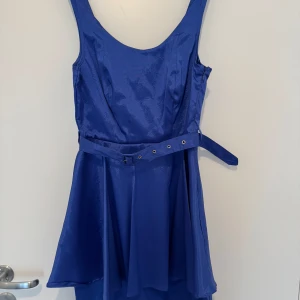 Blå klänning med bälte - Snygg blå klänning med ett matchande bälte i midjan. Klänningen har en rund halsringning och är ärmlös, vilket gör den perfekt för varmare dagar. Den har en dragkedja på sidan för enkel på- och avtagning.