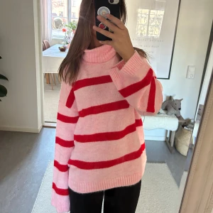 Rosa och röd randig polotröja - Säljer en mysig rosa polotröja med breda röda ränder. Tröjan har långa ärmar och en bekväm passform, perfekt för kyligare dagar. Den är både stilren och färgglad, vilket gör den till ett härligt tillskott i garderoben.