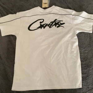 Vit t-shirt från Corteiz - Säljer en vit t-shirt från Corteiz med svart tryck både fram och bak. T-shirten är kortärmad och tillverkad i 100% bomull, vilket gör den bekväm och lätt att bära. Perfekt för en avslappnad stil. Perfekt tröja till sommarn☀️🕶️. Tröjan är true to size, så om du har S så passar den. Helt ny, använd ett par gånger och den är tvättad.