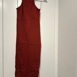 Rostfärgad klänning från NA-KD - Snygg rostfärgad långklänning från NA-KD i ribbat material. Klänningen har en ärmlös design och en stilren look som passar perfekt för olika tillfällen. Perfekt för dig som vill ha en enkel men elegant stil.