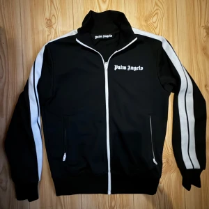 Palm Angels dress set - Snygg svart träningsjacka från Palm Angels. Jackan har en hög krage och loggan på bröstet. Nästintill sprillans nya bara byxorna använt ca 2 gånger. Storlek S på koftan och storlek M på byxorna, sitter riktigt fint! Kvitto och lappar har jag dessvärre inte kvar då den var köpt för 1-2 år sedan, äkthets bevis genom QR-kod finns. Nypris på endast koftan ligger på ca 5400kr!     🌸 Priset är prut bart vid snabb affär