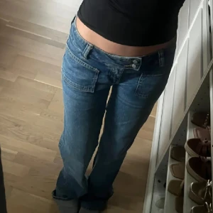 Blå jeans med låg midja - Säljer ett par mörk blå jeans med väldigt låg midja och rak passform. Tror byxan är klassad som straight men sitter ungefär som bootcut eftersom dem sitter bra vid låten men börjar bli större precis över knäna. Har en enkel design med fickor fram och bak samt två knappar och dragkedjestängning. De som är bra me byxan är att den inte är lika låg där bak så man flashas inte när man sitter ner. Köptes för 500kr säljer för 290(:🫶🏼🫶🏼💫som nya