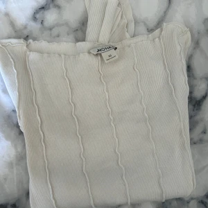 Vit ribbad topp från Monki - Säljer en stilren vit ribbad topp från Monki i storlek XS. Toppen har en offshoulder-design och är tillverkad i ett mjukt material som ger en bekväm passform. Perfekt för att skapa en chic look.