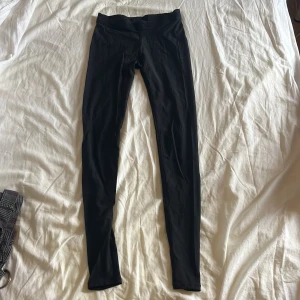 Svarta leggings från SKINS med rosa detalj - Svarta tunna och tajta leggings med en snygg rosa linje längs ena benet. De har bred resår i midjan med logga och är tillverkade i ett stretchigt syntetmaterial som passar perfekt för träning eller chill. Tight passform och stilren look.