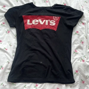 Svart Levi's t-shirt med röd logga - Svart t-shirt från Levi's i bomull med klassisk röd och vit logga framtill. Modellen är kortärmad och har en normal passform. (FLÄCKEN SKA TVÄTTAS BORT INNAN VI POSTAR)