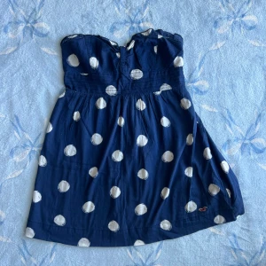 Vintage Marinblå prickig babydoll top Hollister - Söt vintage marinblå babydoll top från Hollister med stora vita prickar. Hade också funkat som miniklänning. Axelbandslös modell med smock upptill för skön passform och lätt utställd kjol. Perfekt för sommarens varma dagar. Tyg i mjuk bomull och diskret Hollister-logga nertill.