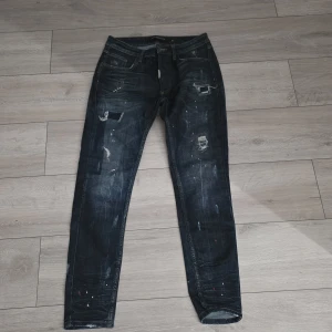 Mörkblå skinny jeans Alessandro Zavetti - Snygga mörkblå skinny jeans från Alessandro Zavetti med slitna detaljer och färgstänk för en cool, streetig vibe. Klassisk femficksmodell i stretchig denim som sitter tajt hela vägen ner. Perfekta för dig som gillar en edgy look.