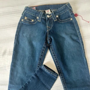 Blåa True Religion jeans - Säljer ett par klassiska blåa jeans från True Religion med ikoniska kontrastsömmar och tydliga bakfickor med logobroderi. Jeansen är i storlek 24