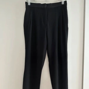 Svarta kostymbyxor - Snygga svarta kostymbyxor med hög avsmalnande ben. Byxorna har pressveck framtill, fickor i sidorna och uppvikta benslut. Perfekta till en clean och stilren look