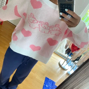 Söt rosa stickad tröja med hjärtan - Supergullig stickad tröja i ljusrosa med stora rosa hjärtan och tre söta kaniner framtill. Tröjan har en loose passform, ribbade muddar och är långärmad. Perfekt för dig som gillar kawaii-stil och vill ha något mysigt och unikt i garderoben.