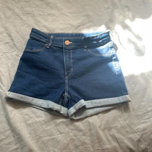 Blå jeansshorts från &Denim - Snygga blå jeansshorts från &Denim med klassisk femficksdesign och uppvikta benslut. Shortsen har normal passform, bälteshällor och synliga kontrastsömmar. Perfekta för varma dagar och enkel att matcha med allt.