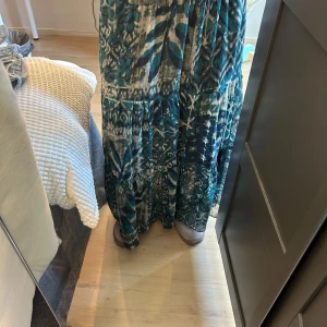 Mönstrad långkjol i blå toner, M - Säljer en  långkjol med fint blått och grönt mönster. Kjolen har resår i midjan och flera lager för extra volym. Perfekt för dig som gillar boho-vibe och vill sticka ut med färg och mönster.