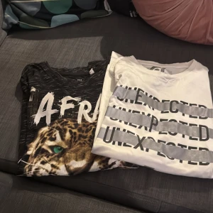 Två coola t-shirts med tryck - Säljer två t-shirts: en svart med leopardtryck och texten 'AFR', samt en vit med gråa ränder och texten 'UNEXPECTED' upprepat. Båda har rund hals och korta ärmar. Perfekta för dig som gillar statement-plagg och djurmönster.