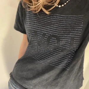 Svart t-shirt med LOVE-tryck - Svart t-shirt med korta ärmar och boxig passform. Framsidan har ett stort fyrkantigt tryck med ordet LOVE i svarta bokstäver och små silvriga prickar runtom. Mjuk bomullskänsla och rund halsringning. Perfekt till jeans eller shorts.