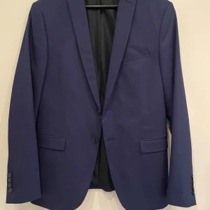 Marinblå kavaj från Zara Man - Snygg marinblå kavaj från Zara Man i klassisk modell med två knappar framtill, fickor med lock och slät baksida. Fodrad insida och stilren passform, perfekt till skjorta och byxor. Storlek 52. Sista bilden ger en mer rätt bild av färgen. 