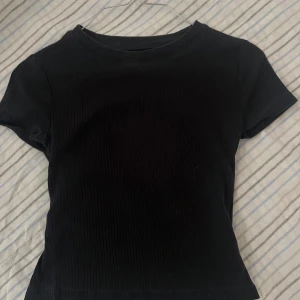 Svart ribbad topp från H&M - En svart ribbad topp från H&M Basic i ekologisk bomull. Modellen har korta ärmar och rund halsringning, perfekt för en enkel och clean look. Materialet är mjukt och stretchigt för en bekväm passform. Jag skulle säga att den sitter som en S.