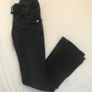 Svarta bootcut jeans med fickor - Snygga svarta low waist jeans med bootcut passform och höga fickor med silverknappar på sidorna. Jeansen har dubbla knappar i linningen. Perfekta för dig som gillar en cool och trendig look.