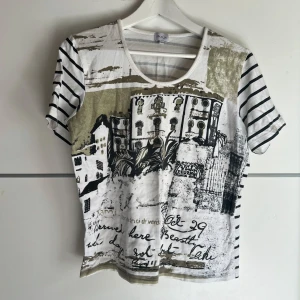 Randig t-shirt med print från Amalia - Cool t-shirt från Amalia i vitt med svarta ränder och ett unikt print framtill med byggnader och text. T-shirten har rund halsringning och korta ärmar. Materialet känns mjukt och skönt, perfekt för en avslappnad stil.