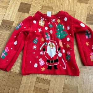 Röd jultröja med tomte från H&M - Supergullig röd jultröja från H&M med tomte, julgran, paket och snöflingor. Tröjan har långa ärmar och är stickad i mjukt material, perfekt för julens alla tillfällen. Färgglada detaljer i grönt, vitt, rosa och gult gör den extra festlig.