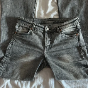 Grå bootcut jeans från Monki - Snygga grå jeans från Monki med bootcut passform och klassisk femficksdesign. Jeansen har en cool tvättad look och är tillverkade i mjukt denimtyg. Perfekta för dig som gillar en retro vibe och vill ha ett par jeans som sticker ut lite extra.