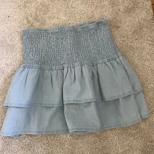 Ljusblå volangkjol med smock - Volangkjol i jeans imitation. Storlek M men passar mig som vanligtvis bär xs eller s. Aldrig använd 
