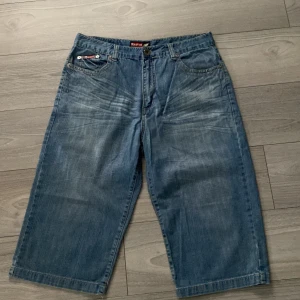 Blå jeansshorts/jorts - Baggy blå jeansshorts med coola detaljer som broderi på bakfickan och klassiska fem fickor. Tillverkade i 100% bomull med normal passform och midwaist. Perfekta för en avslappnad streetstil.