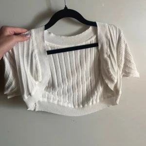 Bolero  - Vit bolero med ribbat mönster och korta ärmar. 