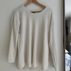 Vit långärmad tröja med slits - En stilren  långärmad tröja med rund halsringning och diskret struktur i tyget. Tröjan har en liten slits i sidorna nedtill för en snygg detalj. 