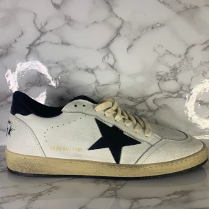 Golden Goose Ball Star sneakers vit/svart - Golden Goose Ball Star sneakers i vitt med svarta detaljer och ikonisk stjärna på sidan. Beige snörning och vintage-inspirerad sula ger en cool retrovibe. Märkets logga syns på hälen och insidan. Perfekta för dig som gillar streetstyle. Kontakta vid minsta lilla fråga! 