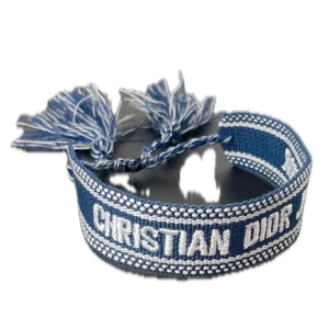 Christian Dior armband - Superfint blått armband från Christian Dior med vit brodyr och texten 'CHRISTIAN DIOR J'ADIOR'. Armbandet har justerbar knytning med flätade band och coola tofsar i blått och vitt. Perfekt accessoar för att lyfta din outfit med en lyxig touch.