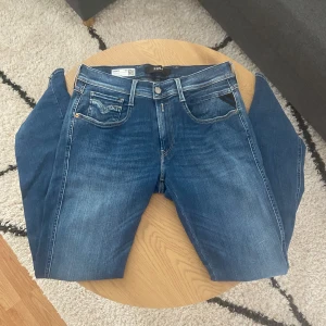 Blåa Replay - Tjena👋 Säljer ett par snygga Replay Anbass jeans i klassisk blå tvätt🙌 Jeansen har fem fickor, vita kontrastsömmar och diskret Replay-logga på bakfickan🪡 Modellen är slim och tillverkad i mjukt bomullsjeansmaterial🧶Perfekta för dig som gillar stilrena och bekväma jeans👖  Storleken är W33(41cm) L34(109cm)📐  Vid frågor: Meddela oss📩