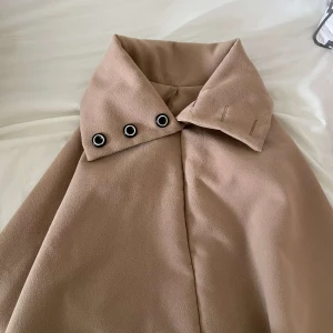 Beige kappa med coola metalldetaljer - Säljer en beige kappa med oversized krage och tre snygga metallöljetter som detalj. Jackan har en stilren och minimalistisk look, perfekt för dig som gillar clean stil. Materialet känns mjukt och lyxigt, och kappan har långa ärmar.